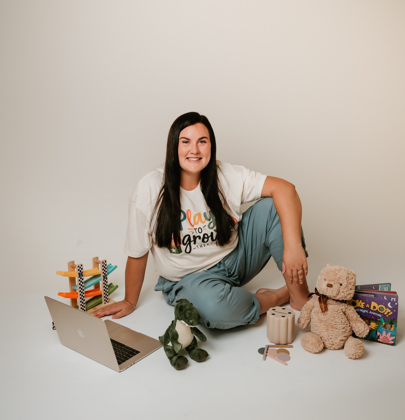 Lauren sitting on the floor surrounded by toys, wearing a Play to Grow Therapy t-shirt